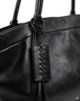 Close-up of the Marais Carryall's whipstitched leather tag and tassel detail in black