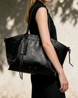 The Marais Carryall in black carried on the shoulder with a black sleeveless dress in sunlight