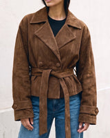 Model wearing the dark brown Margot Tie-waist Coat belted at the waist over a black top and blue jeans, front view