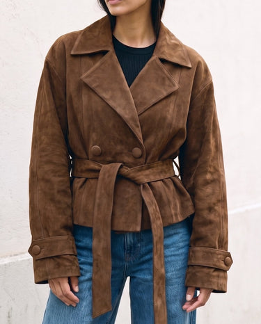 Model wearing the dark brown Margot Tie-waist Coat belted at the waist over a black top and blue jeans, front view