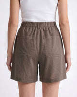 The Mauria Linen Shorts in cocoa — high-waisted pleated linen shorts, back view on model