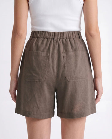 The Mauria Linen Shorts in cocoa — high-waisted pleated linen shorts, back view on model