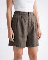 The Mauria Linen Shorts in cocoa — close-up of pleated high-rise waist on model