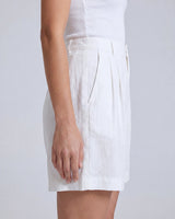 The Mauria Linen Shorts in white — pleated linen shorts, side view on model