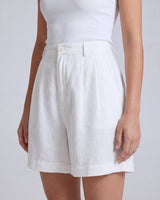 The Mauria Linen Shorts in white — pleated linen shorts, three-quarter view on model