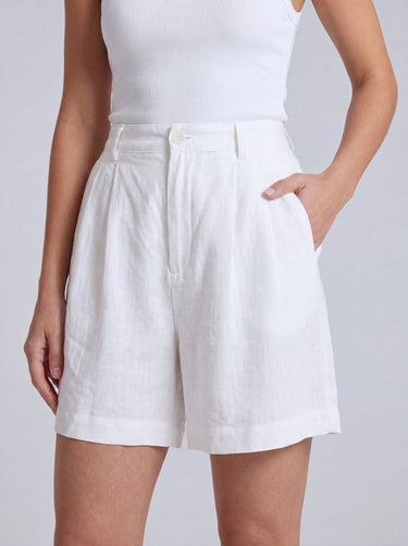 The Mauria Linen Shorts in white — pleated linen shorts with side pockets, hand-in-pocket view on model