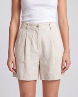 The Mauria Linen Shorts in oat — high-waisted pleated linen shorts, front view on model