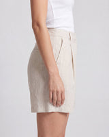 The Mauria Linen Shorts in oat — pleated linen shorts, side view on model