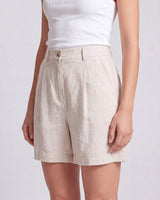 The Mauria Linen Shorts in oat — pleated linen shorts, three-quarter view on model