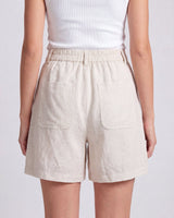 The Mauria Linen Shorts in oat — high-waisted pleated linen shorts, back view on model