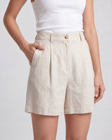 The Mauria Linen Shorts in oat — pleated linen shorts with side pockets, hand-in-pocket view on model