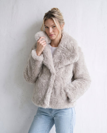 The Noa Faux Fur Coat in beige — faux fur coat, front view on model holding collar