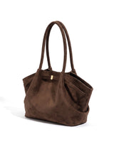 The Odette Suede Tote in brown, three-quarter view showing the winged side pocket and gold-tone keeper