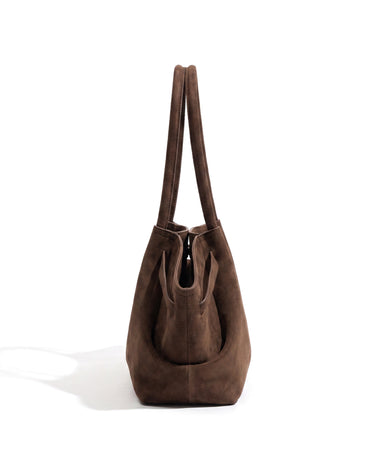 The Odette Suede Tote in brown, side profile view showing the slim depth and folded wing panel
