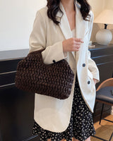 The Ravello Woven Clutch in brown carried under the arm with a cream blazer and floral skirt