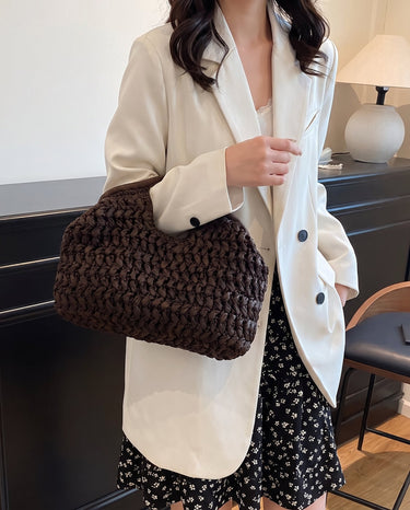 The Ravello Woven Clutch in brown carried under the arm with a cream blazer and floral skirt