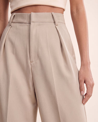 The Riviera Tailored Pants in beige — close-up of pleated waist and pockets