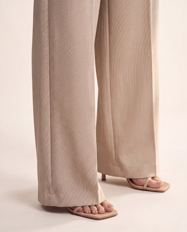 The Riviera Tailored Pants in beige — wide-leg tailored pants, side view on model