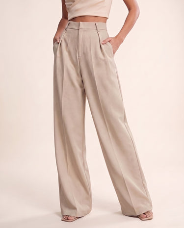 The Riviera Tailored Pants in beige — wide-leg tailored pants with hand in pocket, front view on model