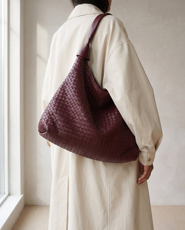 The Siren Woven Bag in burgundy carried on the shoulder with a cream coat
