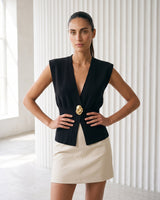 The Solara Gold Button Vest in black — sleeveless knit vest, front view on model with hands on hips