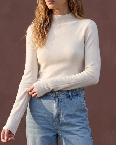 Model wearing pearl white mock-neck knit top with blue jeans, cropped front view – Moriel Heritage