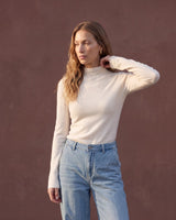 Model wearing pearl white mock-neck knit top with blue jeans, three-quarter view – Moriel Heritage