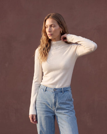 Model wearing pearl white mock-neck knit top with blue jeans, three-quarter view – Moriel Heritage